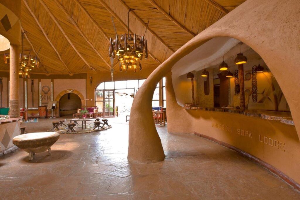 Receptionsdisken i skulpterad lera, med namnet Amboseli Sopa Lodge inristat, under ett tak av vass