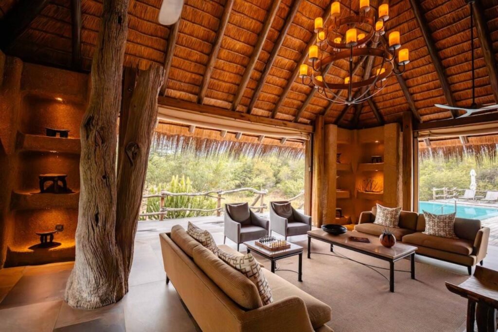 Loungen på Kapama River Lodge under ett högt halmtak, öppen mot en pool och bushen