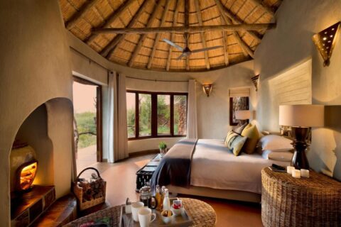 En svit på Madikwe Safari Lodge under ett halmtak, med stor säng och en brasa i den öppna spisen