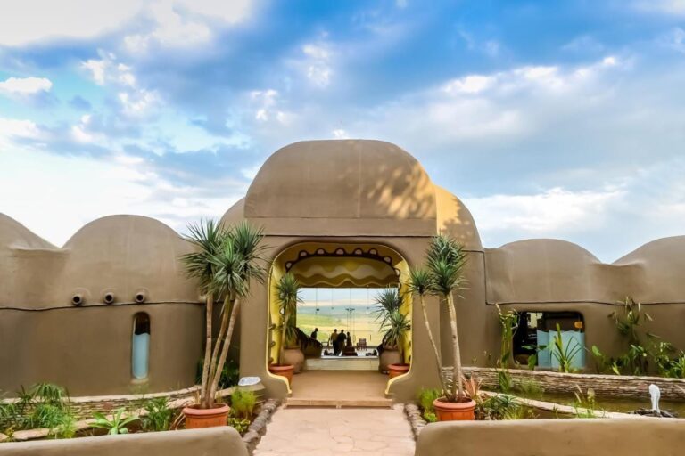 Entrén till Mara Serena Safari Lodge, med kupolformade lerväggar, öppen mot savannen i Masai Mara