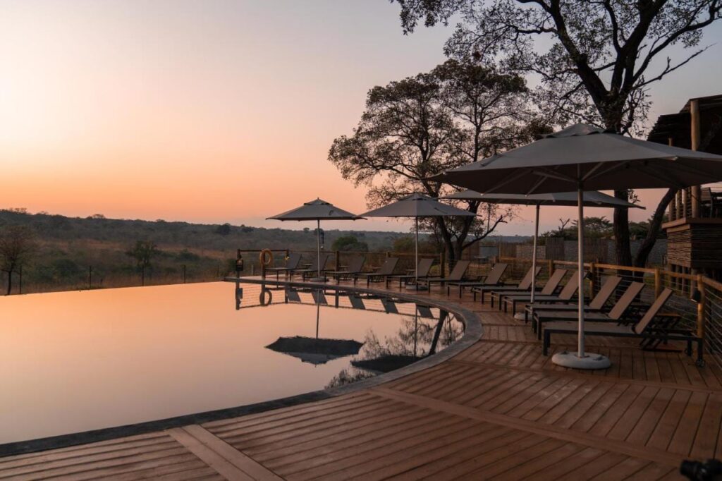 Infinitypoolen på Mdluli Safari Lodge under en orange himmel, kantad av solstolar och parasoller